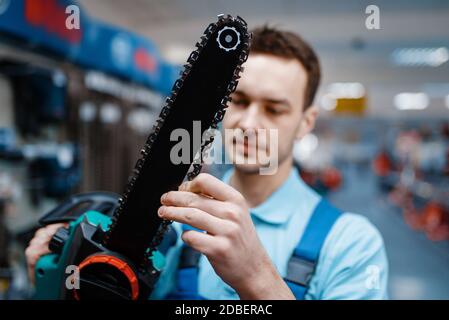 Le travailleur masculin en uniforme tient la scie électrique dans le magasin d'outils. Choix d'équipements professionnels dans la boutique de matériel Banque D'Images