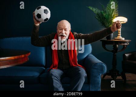 Homme âgé avec foulard rouge et regarder la télévision, fan de football. Poses sénior mûr dans le salon, les personnes âgées sont libres Banque D'Images