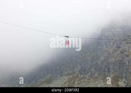 Remontée mécanique rouge dans les nuages et le brouillard, vue latérale à angle bas Banque D'Images
