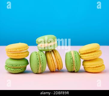 pile de gâteaux ronds d'amande jaune et vert de farine macarons avec crème sur fond bleu, délicieuse pâtisserie Banque D'Images