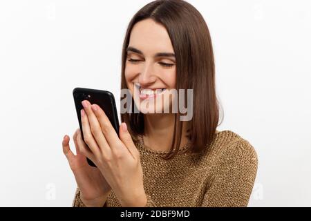 Portrait avant d'une jeune femme souriante utilisant un téléphone portable contre arrière-plan blanc Banque D'Images