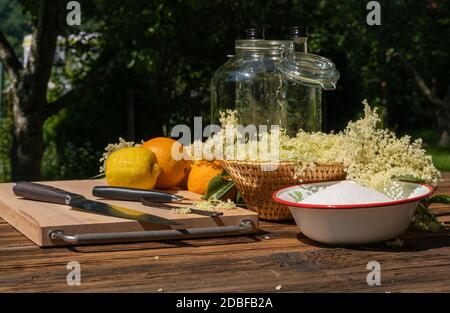 Les fleurs de sureau et autres ingrédients ainsi que les ustensiles de cuisine pour une liqueur de sureau maison sont sur une table en bois dans le jardin Banque D'Images