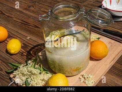 La liqueur de sureau est prête à être fabriquée, tous les ingrédients sont dans le grand pot de conservation, les fleurs de sureau fraîches, les tranches d'oranges et de citron, le sucre, la vanille Banque D'Images