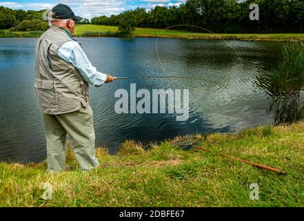 Lincolnshire, Royaume-Uni - M. Barry Grantham, un instructeur de pêche à la mouche, jetant une ligne de mouche à travers un lac de truite pour la truite arc-en-ciel Banque D'Images