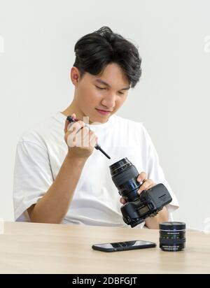 Un photographe asiatique nettoie l'appareil photo et l'objectif avec un appareil photo à soufflerie d'air pour la prise de vue de modèles de mode en studio. Banque D'Images
