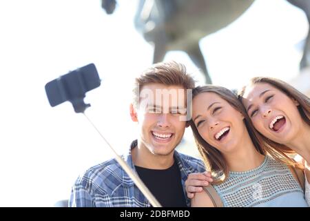 Des amis souriants qui prennent le selfie sur un smartphone avec un bâton en plein air en vacances Banque D'Images