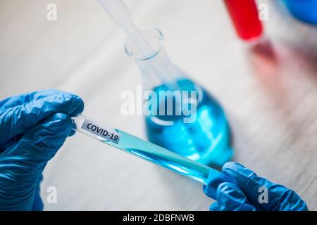 Gros plan sur les mains avec des gants portant un tube à essai Covid-19, en laboratoire. Banque D'Images