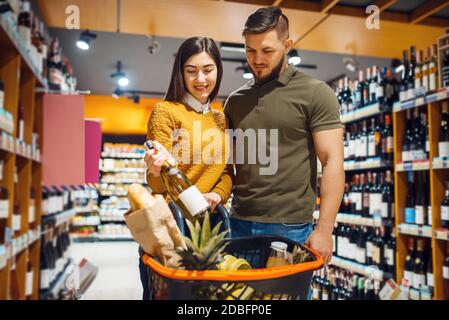 Couple attrayant choix du vin dans le supermarché d'épicerie. Homme et femme avec chariot acheter des boissons sur le marché, les clients acheter de la nourriture et des boissons Banque D'Images