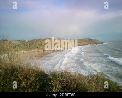 Approche de marée haute à Caswell Bay Beach au pays de Galles, au Royaume-Uni. Vue imprenable sur les vagues qui se brisent sur les rives de sable depuis la Gower Coastal Path vers le soleil Banque D'Images