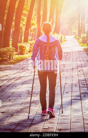 Concept d'aventure et d'exercice de marche nordique - une femme qui fait de la randonnée avec des bâtons de marche nordique dans le parc. Avec évasement de lentille et fuite de lumière Banque D'Images