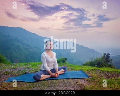Femme sportive pratique le yoga asana Baddha Konasana - angle relié pose à l'extérieur dans les montagnes de l'Himalaya au coucher du soleil. Himachal Pradesh, Inde Banque D'Images