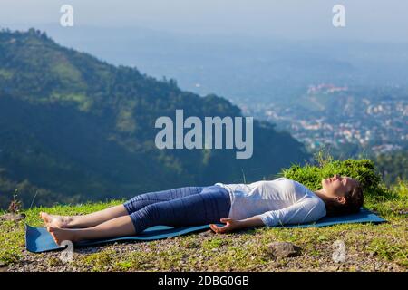 Femme se détend dans le yoga asana Savasana - cadavre pose à l'extérieur dans l'Himalaya. Himachal Pradesh, Inde Banque D'Images