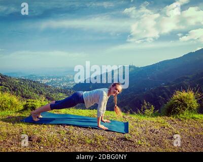 Vintage rétro effet hipster style image de femme faisant Hatha Yoga asana Kumbhakasana plank poser à l'extérieur dans les montagnes Banque D'Images