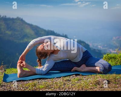 Yoga à l'extérieur - jeune femme sportive faisant du Hatha Yoga asana parivrtta janu sirsasana - posture de la tête au genou tournée - po montagnes le matin Banque D'Images