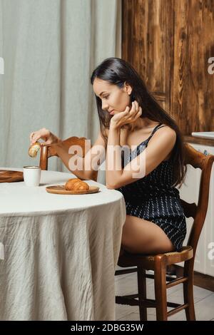 Une femme de race mixte endormie mangeant un croissant frais dans la cuisine le matin Banque D'Images