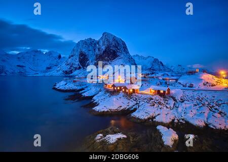 Célèbre attraction touristique village de pêcheurs de Hamnoy sur les îles Lofoten, Norvège avec des maisons de Rorbu rouge dans la neige d'hiver illuminée dans la soirée Banque D'Images