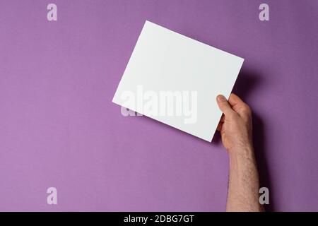 Main de homme tenant un catalogue avec couverture vierge sur fond violet, modèle de série maquette prêt pour votre chemin de sélection de conception inclus Banque D'Images