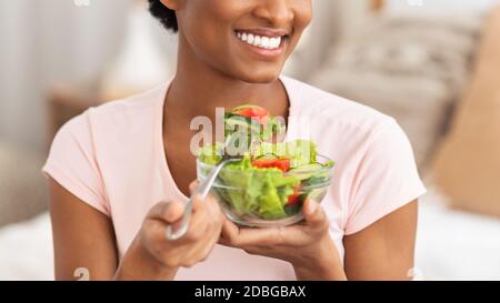 Vue rognée de la jeune femme noire mangeant de la salade de légumes frais à l'intérieur, panorama Banque D'Images