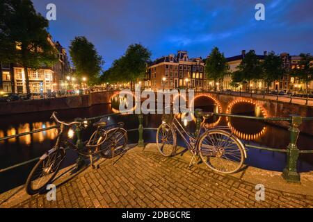 Vue de nuit Amterdam cityscape avec canal, pont avec des vélos et des maisons médiévales dans le crépuscule du soir allumé. Amsterdam, Pays-Bas Banque D'Images
