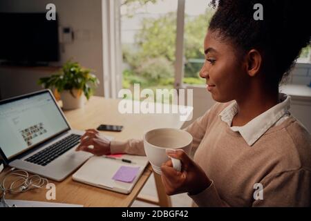 Portrait d'une jeune femme entrepreneur travaillant sur un ordinateur portable à la maison et boire du café Banque D'Images