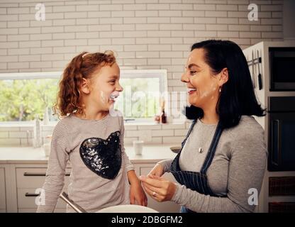 Une femme joyeuse portant un tablier avec sa fille riant et jouant cuisine avec farine sur le visage Banque D'Images