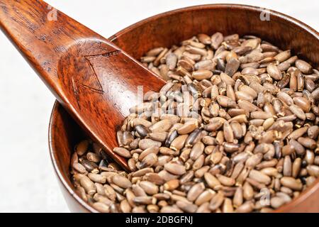 Graines de chardon béni - Silybum marianum - dans une petite tasse en bois avec une pelle sur un tableau blanc, détail gros plan. Banque D'Images