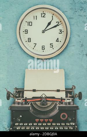 Image de style rétro d'une vieille machine à écrire avec du papier vide feuille et horloge murale Banque D'Images