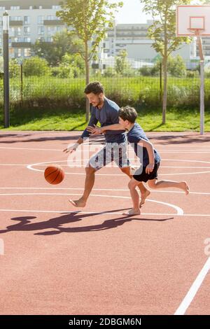 Père et fils jouant au basket-ball pieds nus avec le ballon sur un terrain de jeu Banque D'Images