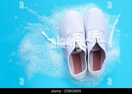 Baskets avec mousse de poudre de détergent eau dissolution sur fond bleu. Lavage des chaussures sales. Vue de dessus Banque D'Images