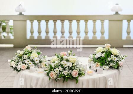 Élégante table de mariage extérieure avec trois posies de rose et des fleurs blanches et des bougies sur un patio en plein air avec balustrade Banque D'Images