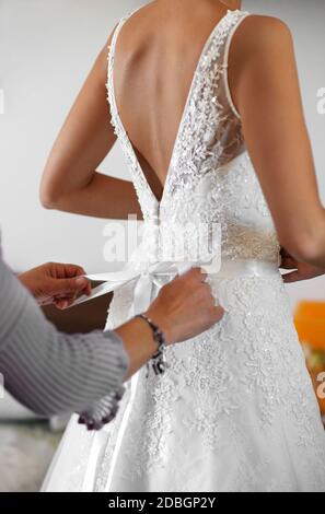 Femme d'honneur aidant la mariée à s'habiller en elle élégante robe de mariée blanche nouant le noeud à l'arrière en gros plan sur ses mains Banque D'Images