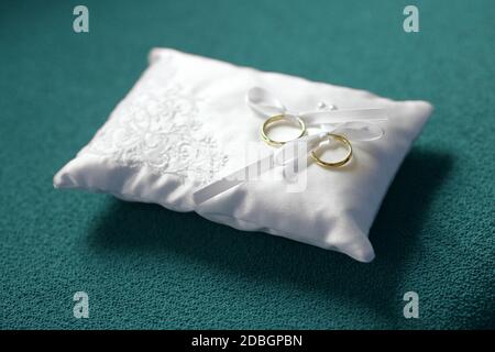 Deux bracelets de mariage dorés avec boucles blanches sur un petit coussin décoratif blanc avant la cérémonie de mariage symbolique d'amour et de romance Banque D'Images