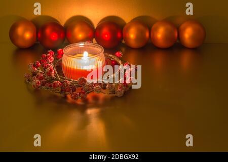 Décoration de Noël avec bougie rouge allumée, couronne de Noël, boules orange et rouge sur fond doré Banque D'Images