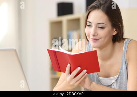 Une femme heureuse lisant des notes sur l'ordre du jour rouge, assise sur un bureau à la maison Banque D'Images