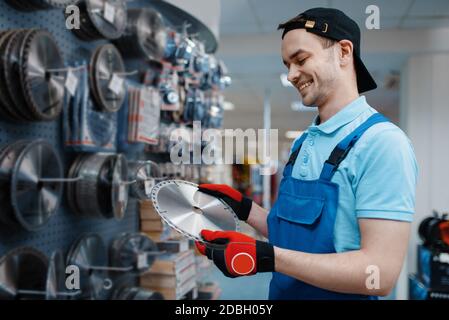 Homme travaillant en uniforme choisir un disque à bords pour la scie dans le magasin d'outils. Choix d'équipements professionnels dans une boutique de matériel, un supermarché d'instruments Banque D'Images