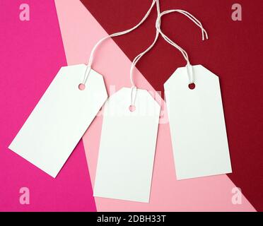 trois étiquettes rectangulaires en papier blanc sur une corde sur un fond coloré, plat. Étiquette de prix, cadeau, pour l'adresse écrite Banque D'Images
