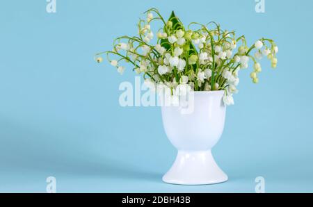 Un bouquet de lys de la vallée dans un œuf tenez-vous debout sur un fond bleu Banque D'Images