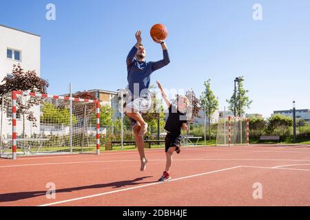 Papa et fils jouant au basket-ball pieds nus avec le ballon sur un terrain de jeu Banque D'Images