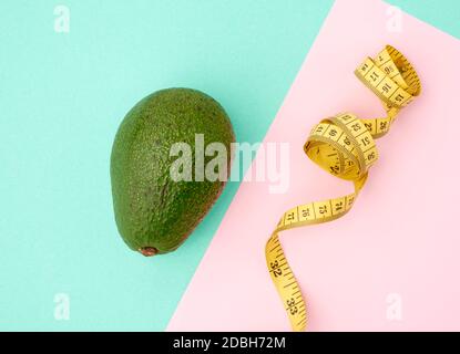 fruit vert avocat et ruban de mesure jaune torsadé sur fond rose vert, concept de régime et de perte de poids, vue du dessus Banque D'Images