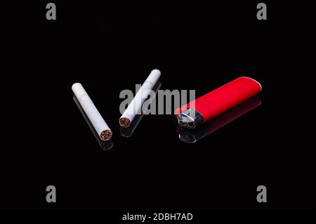 deux cigarettes blanches filtrantes et un briquet rouge gaz plastique sur un fond noir isolé avec réflexion Banque D'Images