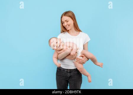 Une jeune mère heureuse et un petit garçon dans une couche, une famille s'amusant ensemble sur un fond bleu isolé Banque D'Images