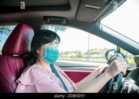 Jeune femme dans un masque de protection et voiture de conduite sur la route Banque D'Images
