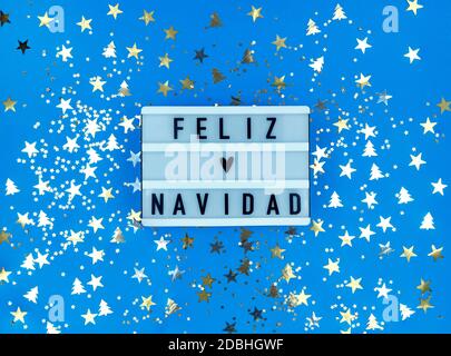 Boîte lumineuse avec phrase de Feliz Navidad, espagnol Joyeux Noël sur fond bleu avec confetti. Banque D'Images