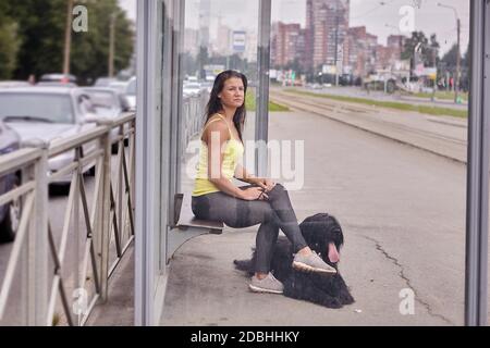 Femme et briard noir à poil long à l'arrêt de tramway. La jeune femme est assise avec son chien à la gare des transports en commun pendant la journée. Banque D'Images