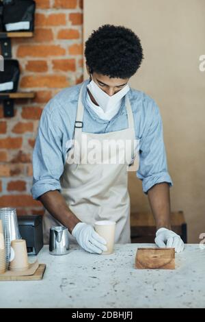 Le barista en gants médicaux prépare du cappuccino au café après la quarantaine Banque D'Images