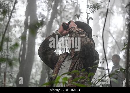 (201117) -- HAIKOU, 17 novembre 2020 (Xinhua) -- UN arpenteur de gibbon observe avec des jumelles dans les forêts tropicales humides de la montagne Bawangling, dans la province de Hainan, au sud de la Chine, le 16 novembre 2020. Connus comme les primates les plus rares au monde, Hainan gibbons augmente en nombre grâce à un environnement amélioré. Les dernières données du département forestier de la province indiquent que 33 gibbons vivent dans cinq familles, soit une triple augmentation de la population des années 1970. Les singes à crête noire ne se trouvent que dans la réserve naturelle nationale de Bawangling, sur l'île Hainan. Ils vivent dans des arbres de la forêt tropicale de plus de 10 mètres Banque D'Images