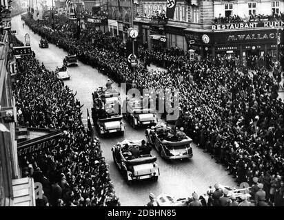 Hitler au milieu de la population viennoise qui applaudit à son entrée à Vienne après l'Anschluss d'Autriche en 1938, suivi d'une escorte avec le personnel de sécurité qui a sauté des voitures à chaque arrêt, le soi-disant Fuehrerbegleitkommando (Fuehrer Escort Command). Banque D'Images