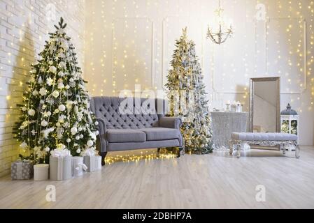 Décoration de Noël élégante dans le salon avec un canapé gris, deux arbres de Noël et guirlandes au mur Banque D'Images