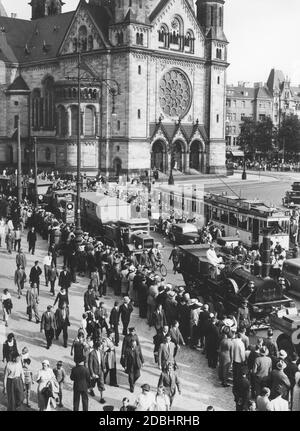 'La réplique du premier train allemand ''Adler'' (locomotive et wagons) a été tirée à travers Berlin vers le parc des expositions de Kaiserdamm le 11 juillet 1936. Il a ensuite attiré les visiteurs à l'exposition 'Deutschland' à travers le terrain en plein air. Sur cette photo, le convoi de camions Deutsche Reichsbahn va directement de Budaapester Strasse à Hardenbergstrasse, en passant par l'église du souvenir de l'empereur Guillaume, sous la surveillance de spectateurs sur le côté de la route. Des publicités pour ''AGB Stoffe'' et ''BMW'' sont accrochées aux lampadaires.' Banque D'Images