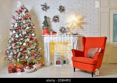 Décoration de Noël douillette dans la salle de séjour avec fauteuil rouge, arbre de Noël et guirlandes Banque D'Images